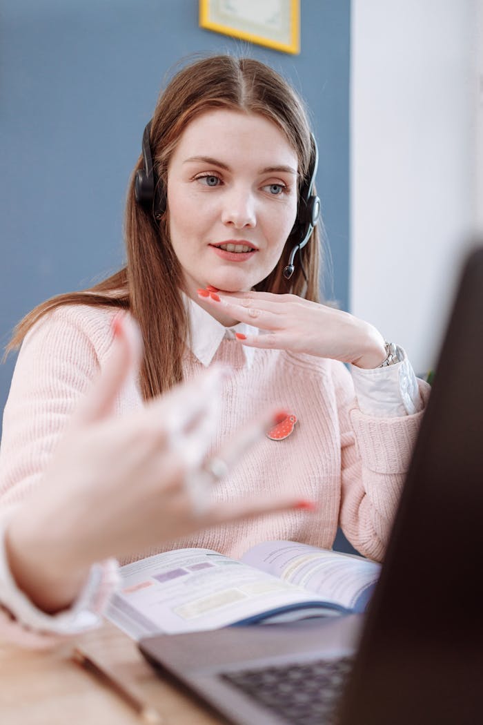 Woman wearing headset teaches online using a laptop from home, engaging in a virtual lesson.